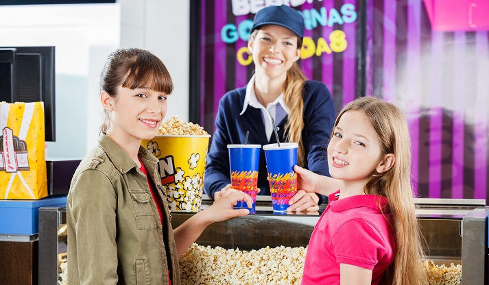 Smiling Girls Buying Popcorn And Drinks From Seller At Cinema