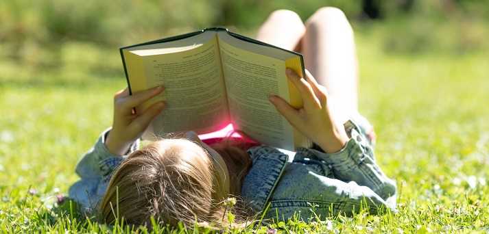 A girl is lying and reading her favorite book on a green meadow covered with yellow flowers on a sunny summer-spring day.