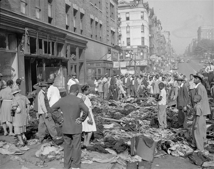 Bystanders gather to look over a pile of merchandise scattered over the sidewalk in front of a pawnshop at 145th Street and Eighth Avenue August 2 1943 an aftermath of Harlem disorders in New York