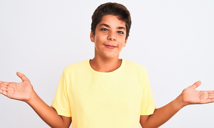 teenage boy standing over white isolated background, clueless and confused expression with arms and hands raised