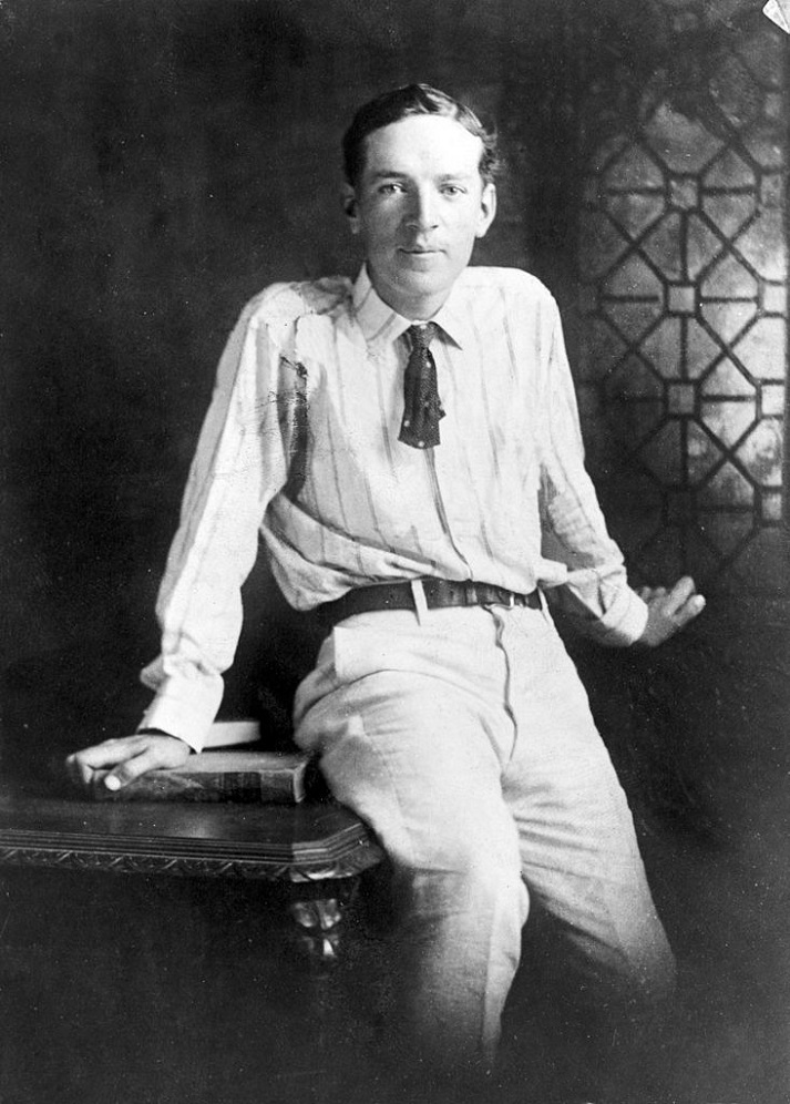 Upton Sinclair, three-quarter length portrait, seated on desk, facing front